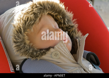 Bambino di undici mesi addormentato nel sedile di vettura dopo il viaggio al parco giochi giacca calda e il cofano Gennaio Foto Stock