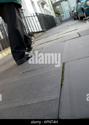 Chiudere i dettagli delle gambe e dei piedi di un uomo che cammina su Welsh Slate bramma marciapiede Aberystwyth Wales UK Foto Stock