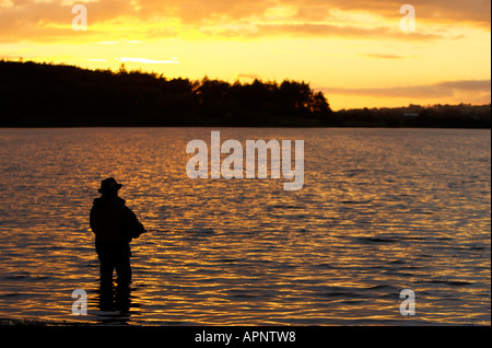 Pescatore di Pesca a Mosca Report di Pesca sul serbatoio Stoneyford al tramonto nella contea di Antrim Irlanda del Nord Foto Stock