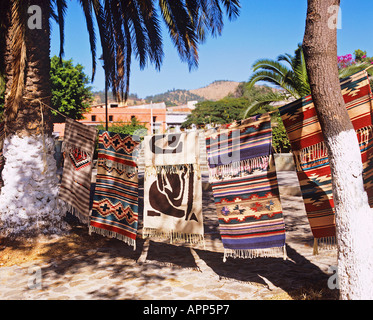 Tessuti a mano tappeti appesi tra alberi di palma in vendita presso la capitale dello stato di Oaxaca Foto Stock