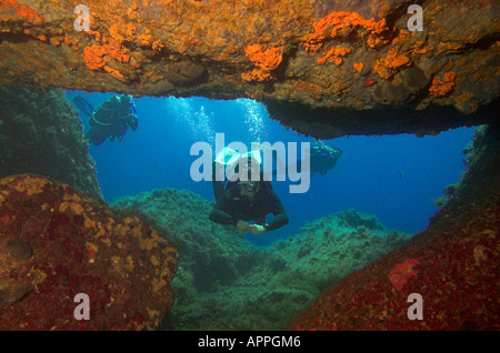 Scuba Diver underwater da ingresso alla grotta con spugne colorate sulle pareti isola di Creta Grecia Foto Stock