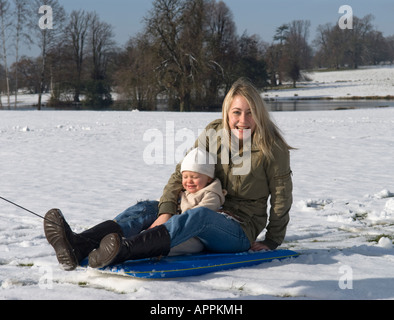 la madre e il figlio di un anno si divertono sulla neve su una slitta, vestiti con caldi abiti invernali Foto Stock