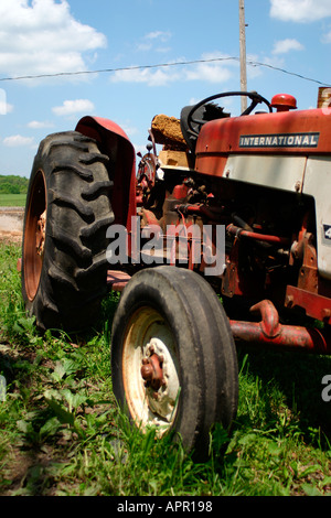 Il trattore farm raccolto nessun'altra attrezzatura zappa rurale erba verde blu cielo nuvole pneumatico rosso antico aratro antiquate John deer falciatrice Foto Stock