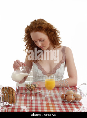 Giovane donna seduta al tavolo per la colazione di frutta e dado muesli con latte toast integrale uova sode succo di arancia Foto Stock