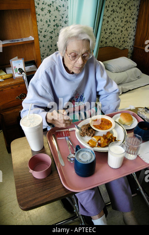 Una femmina senior riceve assistenza da parte di essere servito il cibo e i pasti in una casa di cura il centro di riabilitazione Foto Stock