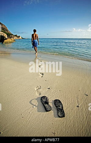 Donna camminare in spiaggia al mare le scarpe e le orme Modello rilasciato Anse Source d Argent beach La Digue Island Seychelles Foto Stock