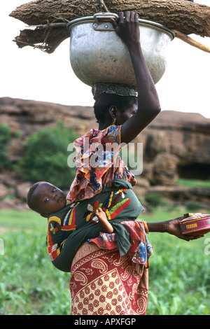 Giovane donna Peul con un bambino legato al suo indietro il bilanciamento di una pentola di metallo sul suo capo Foto Stock