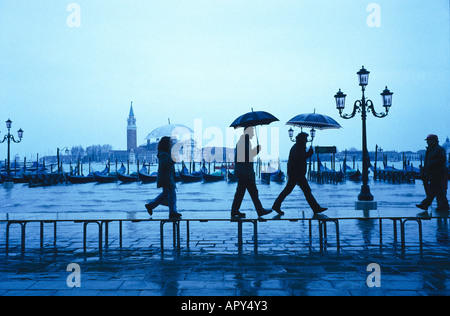 Le persone sono a piedi sotto la pioggia oltre l'allagato Gorgio Maggiore a Venezia, Italia Foto Stock