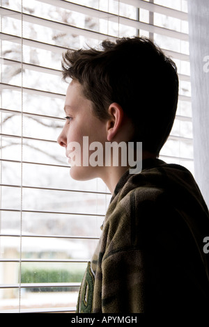 Un ragazzo caucasico di 13 anni che appare triste e solitario si trova di fronte a una finestra che guarda fuori. USA. Foto Stock