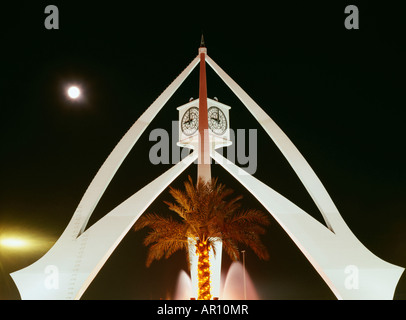 Un illuminato Palm tree è visto al centro di una struttura conica con orologi in cima. Foto Stock