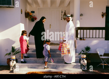 Una famiglia si gira e guarda la telecamera prima di entrare nella casa. Foto Stock