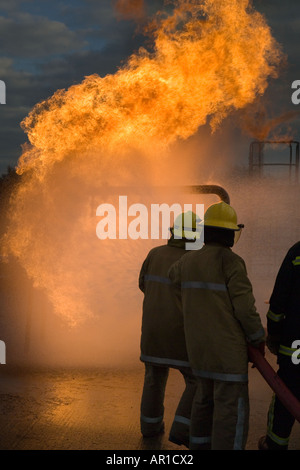 I vigili del fuoco facendo avanzare il fuoco dietro il tubo flessibile di acqua di protezione dello schermo Foto Stock