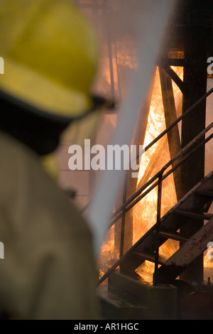 I vigili del fuoco facendo avanzare il fuoco dietro il tubo flessibile di acqua di protezione dello schermo Foto Stock