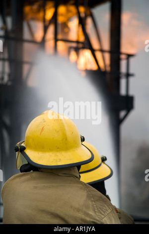 2 per i vigili del fuoco in giallo cappelli avanzando il fuoco dietro il tubo flessibile di acqua di protezione dello schermo Foto Stock