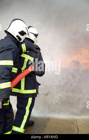 I vigili del fuoco facendo avanzare il fuoco dietro il tubo flessibile di acqua di protezione dello schermo Foto Stock