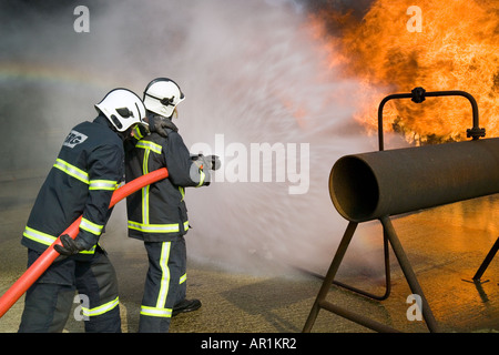 I vigili del fuoco facendo avanzare il fuoco dietro il tubo flessibile di acqua di protezione dello schermo Foto Stock