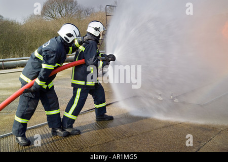 I vigili del fuoco facendo avanzare il fuoco dietro il tubo flessibile di acqua di protezione dello schermo Foto Stock