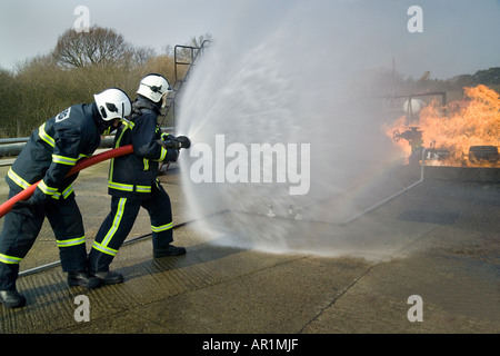 I vigili del fuoco facendo avanzare il fuoco dietro il tubo flessibile di acqua di protezione dello schermo Foto Stock