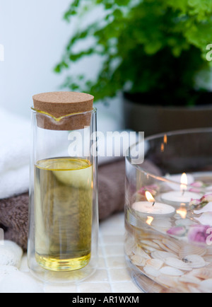 Impostazione di Spa con candele galleggianti e petali di rosa fresca in una ciotola di vetro, asciugamani piegati e olio per massaggi (olio di mandorle dolci) Foto Stock