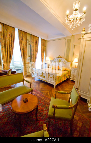 Camera di lusso con letto queen size Beaune Francia | BEAUNE, Francia - Un letto queen size dorato e un'area soggiorno ancora una camera d'epoca all'Hotel le CEP nel cuore della regione vinicola della Borgogna. Il pavimento in parquet a spina di pesce, il lampadario di cristallo e gli arredi ispirati a Luigi XV riflettono le radici dell'hotel in un gruppo di case rinascimentali restaurate nella città vecchia di Beaune. Foto Stock