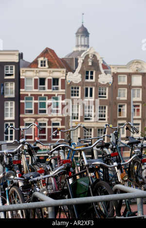 HOLLAND AMSTERDAM Biciclette parcheggiate nel MULTIPIANO BIKE PARK VICINO STAZIONE FERROVIARIA CENTRALE CON vecchi edifici a capanna IN BACKGROUND Foto Stock