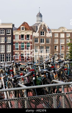 HOLLAND AMSTERDAM Biciclette parcheggiate nel MULTIPIANO BIKE PARK VICINO STAZIONE FERROVIARIA CENTRALE CON vecchi edifici a capanna IN BACKGROUND Foto Stock