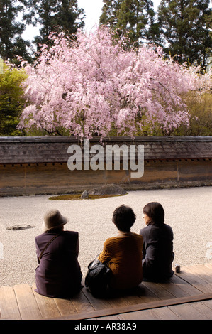 Visitatori sedersi e guardare al giardino di RyoanJi a Kyoto in Giappone durante la fioritura dei ciliegi stagione Foto Stock
