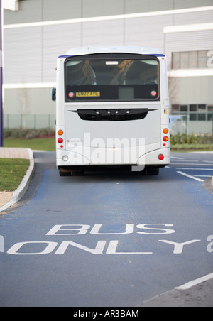 Un colpo di una strada segnata "bus" solo in primo piano con un bus che si avvicinano ad un grande edificio industriale Foto Stock