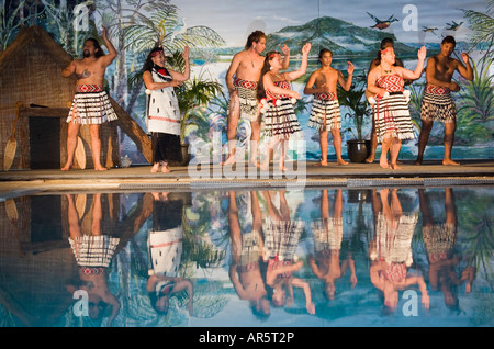 Persone che svolgono tradizionale Maori intrattenimenti danzanti sul palco riflesso in acqua di piscina Kapa Haka Nuova Zelanda Foto Stock