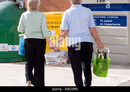 Coppia senior camminando mano nella mano che trasportano contenitori di bottiglie per buttare nel cestino Foto Stock