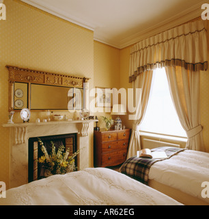 In stile georgiano specchio sopra il camino in camera da letto con due letti singoli e orlata mantovane sulle tende di color crema Foto Stock