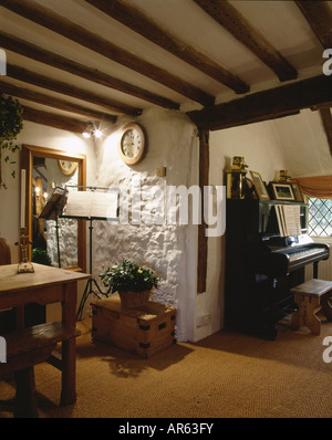 Il pianoforte e il music stand in cottage hall con tappeto in sisal e travi a soffitto Foto Stock