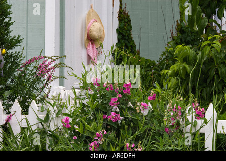 Cappello di paglia appeso sulla porta del capannone in un colorato giardino nel cortile Foto Stock