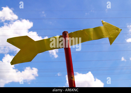 Rosso e giallo freccia di metallo contro un profondo nuvoloso cielo blu criscrossed parallelamente da linee di alimentazione. Foto Stock