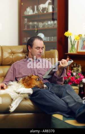 Uomo seduto sul divano con il cane rivista di lettura Foto Stock