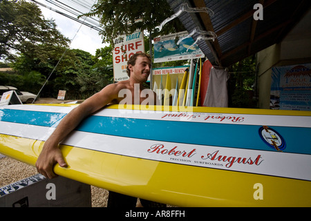 Un surfista porta una tavola da surf Robert August in un negozio di surf a Tamarindo, Guanacaste, Costa Rica Foto Stock