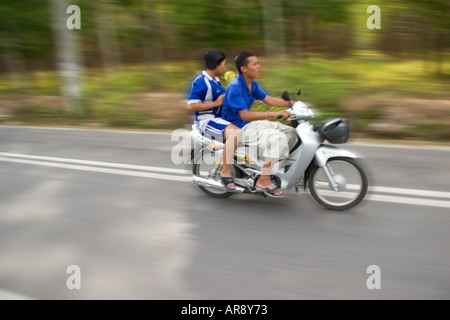 Maschio e femmina a cavallo su un ciclomotore scooter veloce lungo una strada di piantagione sull'Isola di Phuket, Thailandia, Asia Foto Stock