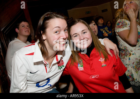 Due giovani donne uno un sostenitore in Inghilterra le altre una ventola del Galles guardare la partita di rugby insieme nel pub - Il Galles vinse 26-19 Foto Stock