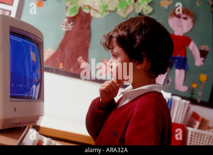 1990 's Infant Boy 3-5 anno. Prima classe di computer bambino di scuola di 1a elementare guarda il terminale dello schermo del computer del 90 con opere d'arte scolastiche visualizzate in b/g. Foto Stock