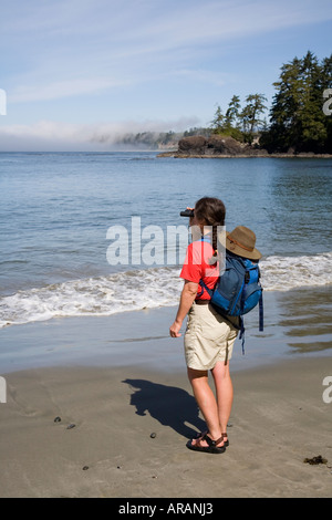 Walker con zaino in spalla usiing binocolo sulla spiaggia con mare di nebbia in background Halfmoon Bay Pacific Rim isola di Vancouver in Canada Foto Stock