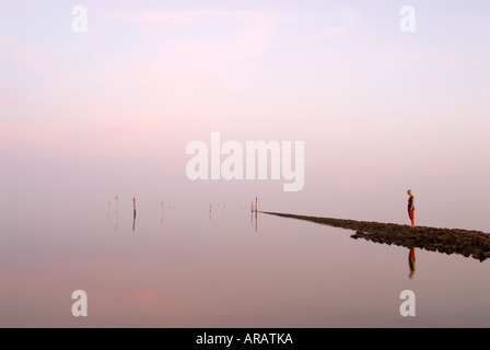 La riflessione della persona in piedi sul molo di pietra nel mare di Wadden, Juist, il Wadden Sea national park, Germania Foto Stock