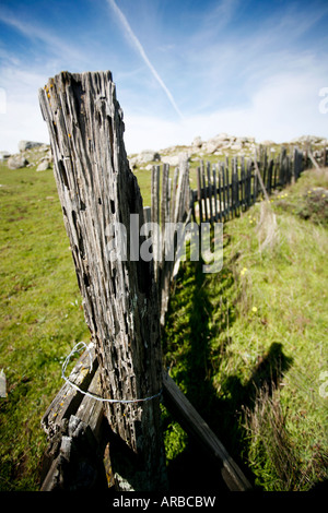 Consumato staccionata in legno lungo un poggio erboso con grandi massi in background Foto Stock