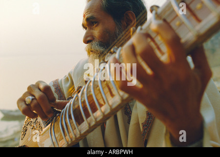 Uomo anziano giocando il sitar accanto al Gange Ganga (Fiume), Varanasi (Benares), nello Stato di Uttar Pradesh, India Foto Stock