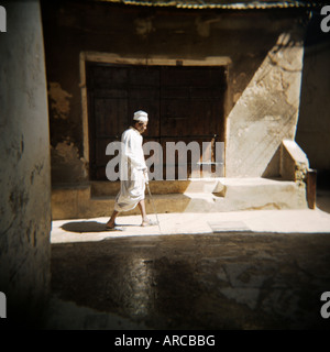 Il vecchio uomo che cammina verso il basso loschi strada nelle tradizionali vesti bianche, Stone Town Zanzibar, Tanzania, Africa orientale, Africa Foto Stock