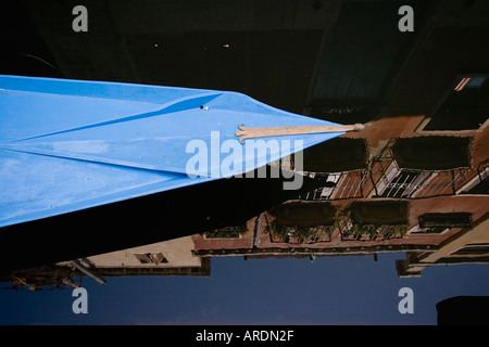 Prua di blu dipinto di imbarcazione in legno con mattoni di edificio residenziale si riflette nelle calme acque del Canal Venezia Italia Foto Stock