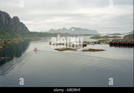 Una piccola barca da pesca di lasciare il porto di Svolvaer passato una fila di rosse tradizionali cabine di legno Foto Stock