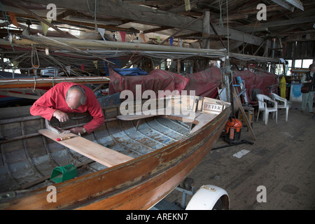 Uomo che ripara una piccola barca di legno in cantiere tradizionali, Woodbridge, Suffolk, Inghilterra Foto Stock