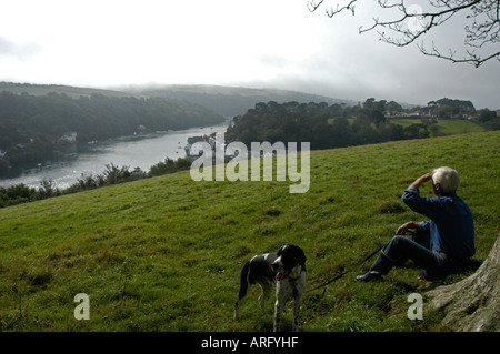 Un uomo e il suo cane sedersi sulla collina che domina la città di Fowey in sud Cornwall Regno Unito Foto Stock