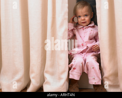 Bambina sul telefono dietro la cortina Foto Stock