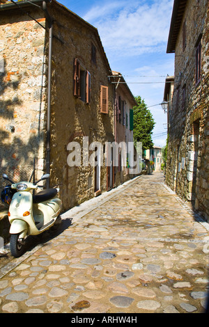 Un motore scooter è parcheggiato su ciottoli in una corsia deserta con case su entrambi i lati nel villaggio Toscano di Monteriggioni. Foto Stock